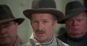 Movie still from “Salò, or the 120 Days of Sodom” (1975), directed by Pier Paolo Pasolini – A person wearing a hat and a tie; Close Up shot, Low angle