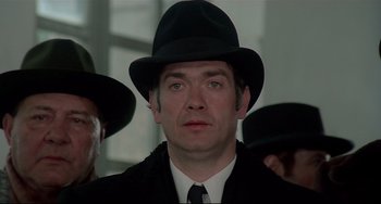 Movie still from “Salò, or the 120 Days of Sodom” (1975), directed by Pier Paolo Pasolini – A person wearing a suit and a hat; Close Up shot, Low angle