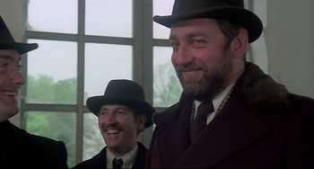 Movie still from “Salò, or the 120 Days of Sodom” (1975), directed by Pier Paolo Pasolini – Two men in suits and hats smiling for the camera in front of a window; Close Up shot, Low angle