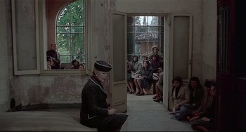 Movie still from “Salò, or the 120 Days of Sodom” (1975), directed by Pier Paolo Pasolini – A group of people sitting and standing in a room; Wide shot, Over the shoulder angle