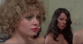 Movie still from “Salò, or the 120 Days of Sodom” (1975), directed by Pier Paolo Pasolini – A woman with curly blonde hair and green eye shadow; Close Up shot, Over the shoulder angle