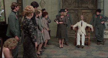 Movie still from “Salò, or the 120 Days of Sodom” (1975), directed by Pier Paolo Pasolini – A group of people standing around a man in a chair; Wide shot, High angle