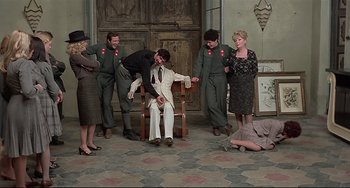 Movie still from “Salò, or the 120 Days of Sodom” (1975), directed by Pier Paolo Pasolini – A group of people standing around a man in a chair; Wide shot, High angle