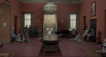Movie still from “Salò, or the 120 Days of Sodom” (1975), directed by Pier Paolo Pasolini – A group of people sitting around a table in a room; Extreme Wide shot, High angle