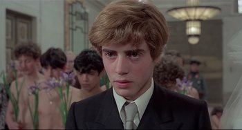 Movie still from “Salò, or the 120 Days of Sodom” (1975), directed by Pier Paolo Pasolini – A man in a suit and tie in front of a group of people; Close Up shot, Over the shoulder angle