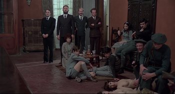 Movie still from “Salò, or the 120 Days of Sodom” (1975), directed by Pier Paolo Pasolini – A group of men and women sitting on the floor of a living room; Wide shot, High angle