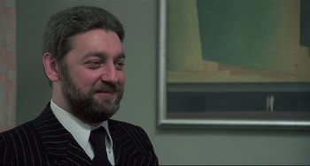 Movie still from “Salò, or the 120 Days of Sodom” (1975), directed by Pier Paolo Pasolini – A man in a suit and tie in front of a painting; Close Up shot, Low angle