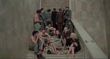 Movie still from “Salò, or the 120 Days of Sodom” (1975), directed by Pier Paolo Pasolini – A group of men and women sitting and standing on steps; Wide shot, High angle