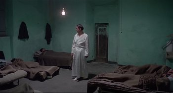 Movie still from “Salò, or the 120 Days of Sodom” (1975), directed by Pier Paolo Pasolini – A man in a white robe standing in a room with two beds; Wide shot, High angle