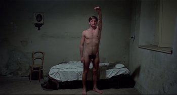 Movie still from “Salò, or the 120 Days of Sodom” (1975), directed by Pier Paolo Pasolini – A naked man standing in a room next to a bed; Medium shot, High angle