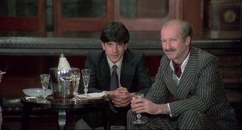 Movie still from “Salò, or the 120 Days of Sodom” (1975), directed by Pier Paolo Pasolini – Two men sitting at a table with a glass of wine in front of them; Medium shot, Low angle