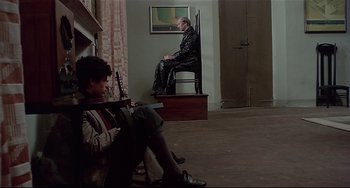 Movie still from “Salò, or the 120 Days of Sodom” (1975), directed by Pier Paolo Pasolini – A man sitting on a chair next to a woman; Wide shot, High angle