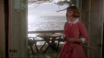 Movie still from “Same Time, Next Year” (1978), directed by Robert Mulligan – A woman in a pink dress standing on a porch near the water; Medium shot, Over the shoulder angle