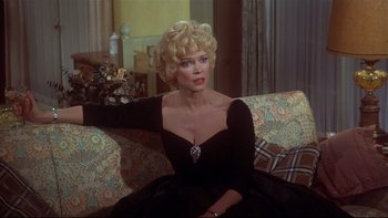 Movie still from “Same Time, Next Year” (1978), directed by Robert Mulligan – A woman sitting on top of a couch wearing a black dress; Medium shot, Over the shoulder angle