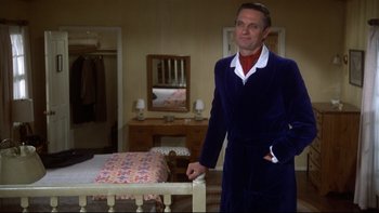 Movie still from “Same Time, Next Year” (1978), directed by Robert Mulligan – A man in a blue robe standing next to a bed in a bedroom; Medium shot, Low angle