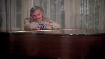 Movie still from “Same Time, Next Year” (1978), directed by Robert Mulligan – A man sitting in front of a piano in front of a window; Medium shot, High angle