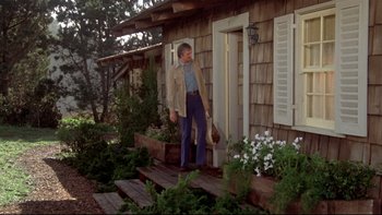 Movie still from “Same Time, Next Year” (1978), directed by Robert Mulligan – A man standing on the steps of a wooden house; Wide shot, Low angle