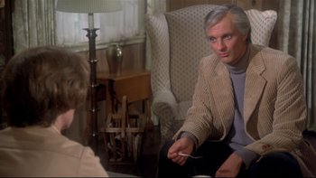 Movie still from “Same Time, Next Year” (1978), directed by Robert Mulligan – A man sitting in a chair holding a cigarette in his hand; Medium shot, Over the shoulder angle