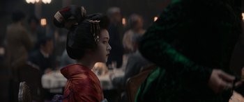 A geisha is sitting at a table in front of a group of people
