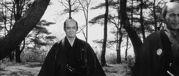 Movie still from “Samurai Rebellion” (1967), directed by Masaki Kobayashi – A man in a black robe standing in front of trees; Medium shot, Low angle