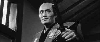 Movie still from “Samurai Rebellion” (1967), directed by Masaki Kobayashi – A black - and - white photo of a man holding a sword; Close Up shot, Low angle