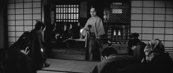 Movie still from “Samurai Rebellion” (1967), directed by Masaki Kobayashi – A man standing in front of an audience in front of a microphone; Wide shot, Low angle