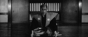 Movie still from “Samurai Rebellion” (1967), directed by Masaki Kobayashi – A man sitting on the ground wearing a kimono; Medium shot, Low angle