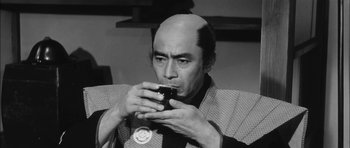 Movie still from “Samurai Rebellion” (1967), directed by Masaki Kobayashi – A man with a bald head drinking a cup of coffee; Close Up shot, Low angle