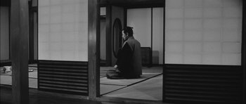 Movie still from “Samurai Rebellion” (1967), directed by Masaki Kobayashi – A man sitting on the ground in front of an open door; Wide shot, Low angle