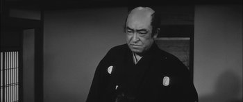 Movie still from “Samurai Rebellion” (1967), directed by Masaki Kobayashi – An older man wearing a black robe and a black hat; Close Up shot, Low angle