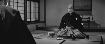 Movie still from “Samurai Rebellion” (1967), directed by Masaki Kobayashi – An older man sitting on the ground in a room; Medium shot, Low angle