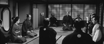 Movie still from “Samurai Rebellion” (1967), directed by Masaki Kobayashi – A group of people sitting in a circle in front of a window; Wide shot, High angle