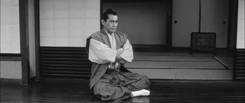 Movie still from “Samurai Rebellion” (1967), directed by Masaki Kobayashi – A man sitting on the ground wearing a robe; Medium shot, High angle