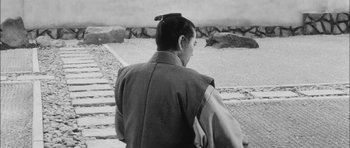 Movie still from “Samurai Rebellion” (1967), directed by Masaki Kobayashi – A man with a long black hair is standing on some steps; Medium shot, High angle