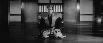 Movie still from “Samurai Rebellion” (1967), directed by Masaki Kobayashi – A man sitting on the ground wearing a kimono; Medium shot, Low angle