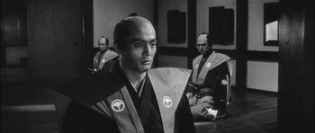 Movie still from “Samurai Rebellion” (1967), directed by Masaki Kobayashi – A black and white photo of a man in a samurai outfit; Medium shot, Over the shoulder angle