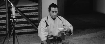 Movie still from “Samurai Rebellion” (1967), directed by Masaki Kobayashi – A man sitting on the ground holding a bowl; Medium shot, High angle