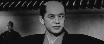 Movie still from “Samurai Rebellion” (1967), directed by Masaki Kobayashi – A man with a shaved head wearing a black jacket; Close Up shot, Low angle