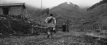 Movie still from “Samurai Rebellion” (1967), directed by Masaki Kobayashi – A man walking down a road with a fence behind him and another man standing in the background; Extreme Wide shot, Low angle