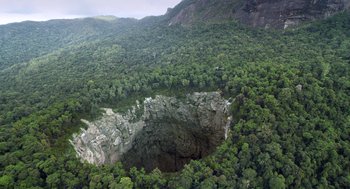 Movie still from “Sanctum” (2011), directed by Alister Grierson – An aerial view of a mountain with trees surrounding it; Extreme Wide shot, Overhead angle