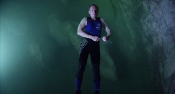 Movie still from “Sanctum” (2011), directed by Alister Grierson – A man standing in the water holding a water bottle; Wide shot, High angle