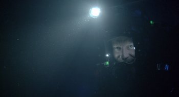 Movie still from “Sanctum” (2011), directed by Alister Grierson – A man in a diving suit with a light in the background; Close Up shot, Overhead angle