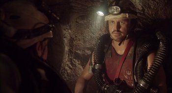 Movie still from “Sanctum” (2011), directed by Alister Grierson – A man in a helmet and a gas mask is in a cave; Medium shot, Over the shoulder angle