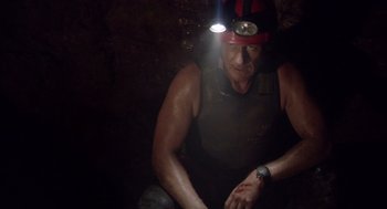 Movie still from “Sanctum” (2011), directed by Alister Grierson – A man with a helmet on his head is sitting in the dark; Medium shot, Low angle