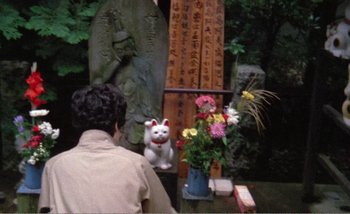 Movie still from “Sans Soleil” (1983), directed by Chris Marker – A statue of a cat in front of a statue; Medium shot, High angle