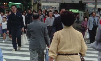 Movie still from “Sans Soleil” (1983), directed by Chris Marker – A group of people walking across a street; Wide shot, High angle
