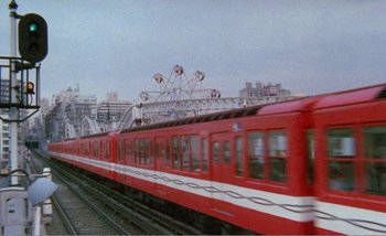 Movie still from “Sans Soleil” (1983), directed by Chris Marker – A red and white train traveling down the tracks; Extreme Wide shot, Low angle