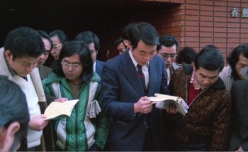 Movie still from “Sans Soleil” (1983), directed by Chris Marker – A group of people standing next to each other holding papers; Medium shot, High angle