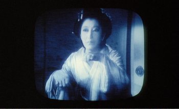 Movie still from “Sans Soleil” (1983), directed by Chris Marker – An old photo of an asian woman in a white dress; Extreme Close Up shot, High angle