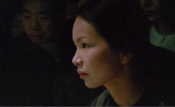 Movie still from “Sans Soleil” (1983), directed by Chris Marker – A young woman looking to her left in the dark; Close Up shot, Over the shoulder angle